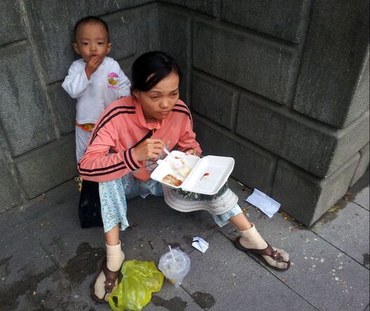Mother and child street people having their meal on the pavement